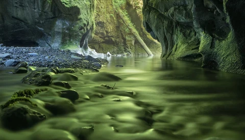 Moss-covered canyon walls frame a flowing stream with silky water captured using long exposure photography.