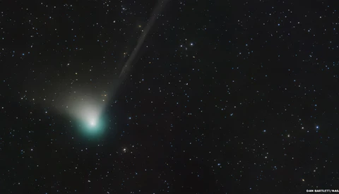 Comet with bright greenish coma and dust tail against starfield.