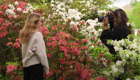 Photographer capturing portrait of woman posing among blooming pink and white flowers.