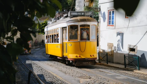 Yellow and cream vintage tram on narrow cobblestone street lined with white buildings.