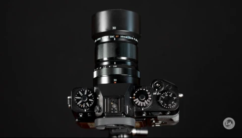 Top-down view of a vintage rangefinder camera with 30mm lens and mechanical controls against black background.