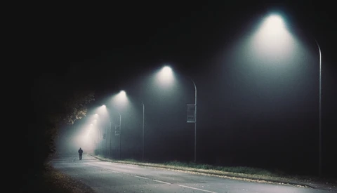 Solitary figure walking down a dark road illuminated by street lamps at night.