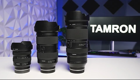 Three Tamron lenses of increasing size arranged left to right, displayed against a blue geometric backdrop with the Tamron logo visible.