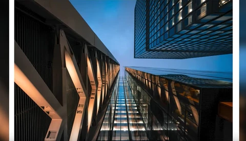 Upward perspective of modern skyscrapers converging toward clear blue sky with warm golden light across facades.