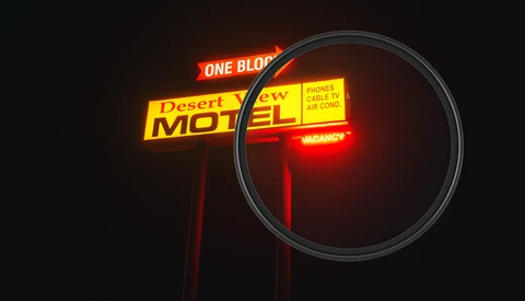 Vintage neon motel sign glowing red and yellow against dark night sky with magnifying glass overlay.