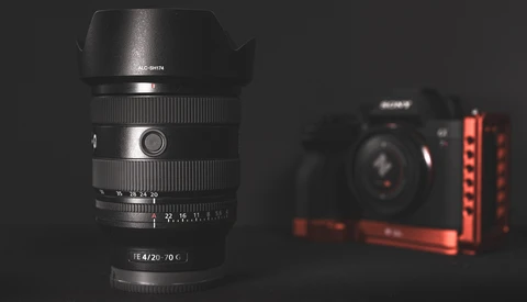 Fast prime lens with f/4.20-70°C specifications displayed on barrel, positioned in sharp focus against blurred camera and red lighting rig.