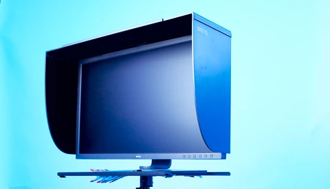 Professional color reference monitor with hood displayed against a cyan background.