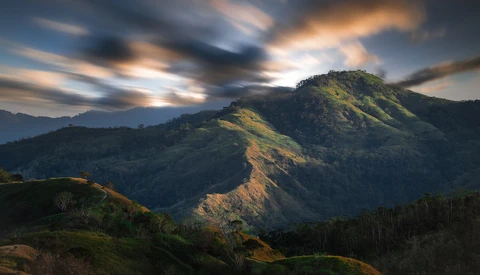 Dramatic mountain landscape with layered peaks bathed in golden sunlight under a moody sky.