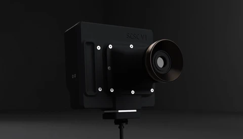 Sleek black cinema camera with prominent lens and white mounting points against dark background.