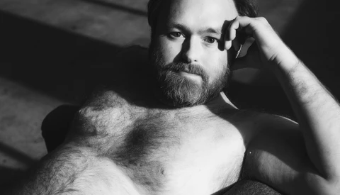 Bearded man in black and white portrait with hand to head, dramatic side lighting.