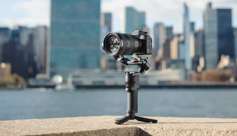 Compact camera gimbal mounted on concrete ledge with blurred cityscape and waterfront in background.