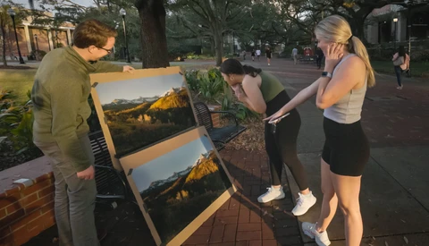 Street photographer displays landscape prints on an easel while passersby examine the work in natural evening light.