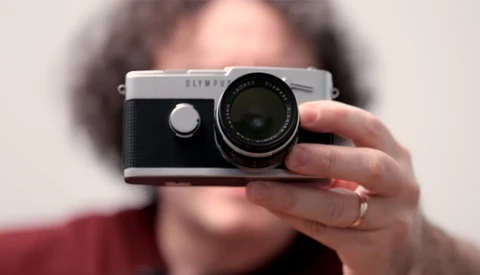 Person holding a rangefinder camera with silver top plate and black body toward the camera.