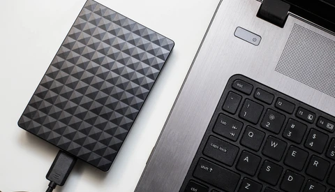 External hard drive with diamond pattern texture positioned next to laptop keyboard on white surface.