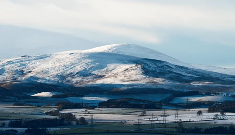 Snow-capped mountain dominating a winter landscape with forested valleys and agricultural fields below.