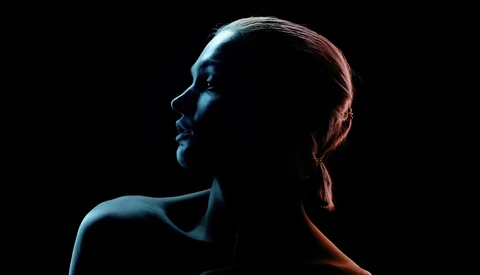Profile of a woman's face and shoulders against a black background with warm and cool colored rim lighting.