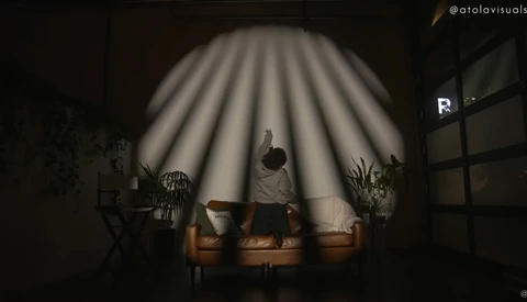 Person sitting on a brown leather couch under dramatic radial light rays in a dark interior space.