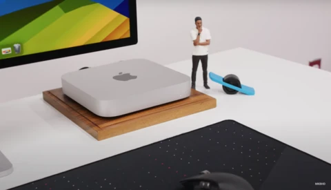 3D render of a Mac mini computer on a wooden base next to a miniature figurine and blue device.