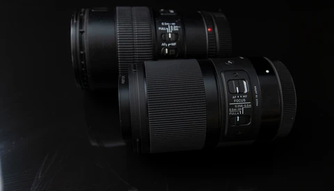 Two black telephoto lenses arranged on a dark surface against a black background.