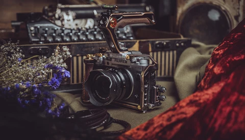 Medium format camera with lens positioned among vintage photography equipment and dried flowers in warm, moody lighting.