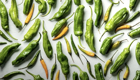 Green and yellow serrano peppers arranged on a white surface.