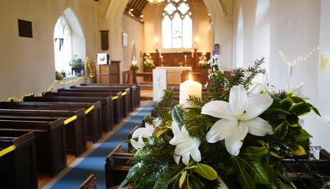 White lilies with greenery arranged in the foreground of a church aisle decorated for a wedding ceremony.