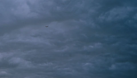 Small aircraft silhouette flying through dramatic storm clouds at dusk.