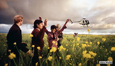 Four children in a wildflower field reaching toward a descending helicopter against a dramatic cloudy sky.