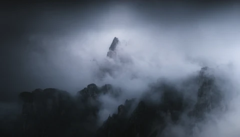 Dramatic mountain peaks shrouded in dense fog and mist under a moody gray sky.
