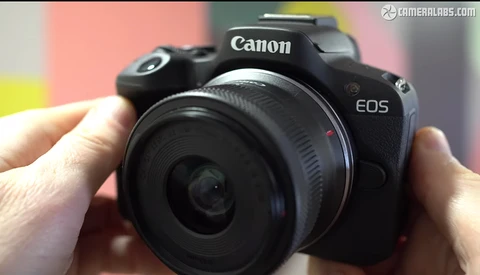 Canon EOS mirrorless camera held in hands against a colorful background.