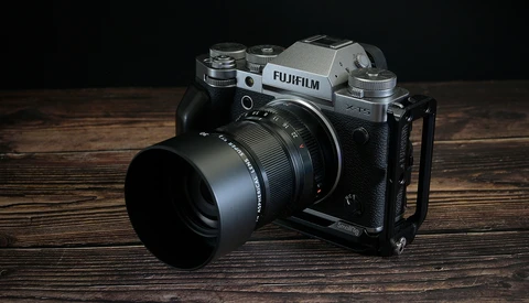 Fujifilm X-T4 mirrorless camera with lens and hood on wooden surface.