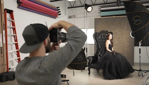 Photographer shooting a portrait subject seated in an ornate black chair in a professional studio setup.