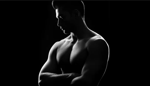 Shirtless male figure in profile against black background, dramatically lit to emphasize musculature.