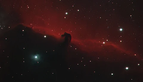 The Horsehead Nebula, a dark dust cloud silhouetted against glowing red hydrogen gas with scattered stars throughout the field.