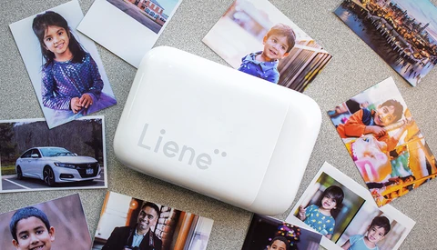 Portable photo printer surrounded by printed photographs on a textured surface.