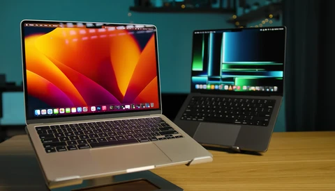 Two laptops on a wooden table displaying video editing software with colorful waveforms and timelines.