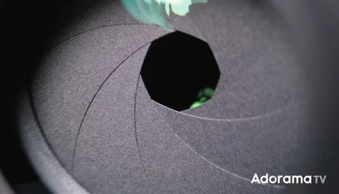 Close-up of a camera aperture blade assembly with a bright green eye visible through the opening.