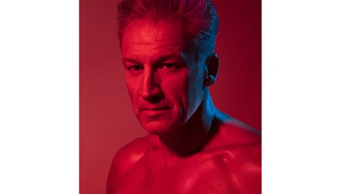 Portrait of a man with styled hair against a red and blue split-tone background.