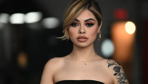 Portrait of a woman with short blonde hair and shoulder tattoo against blurred nighttime background.