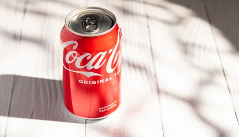 Red Coca-Cola Original can with pull-tab top on white wooden surface with dappled shadow.