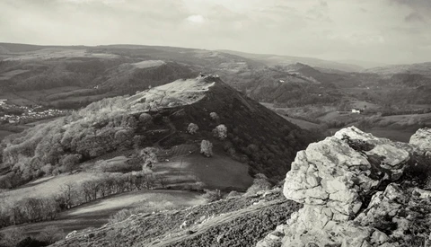 Rocky outcrop in foreground with forested hills and agricultural valleys stretching across a misty landscape.