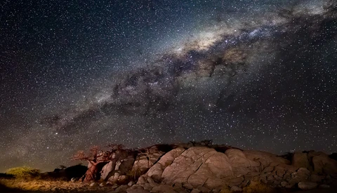 Milky Way galaxy stretching across night sky above desert rock formations.
