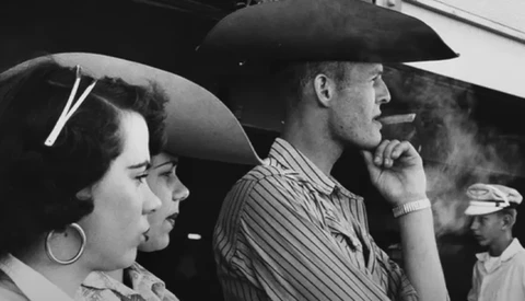 Black and white photograph of people in a vehicle, with a man in a cowboy hat smoking a cigar in profile.