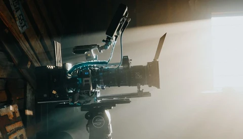 Professional cinema camera with mounted lens and shoulder rig setup lit by bright window light.