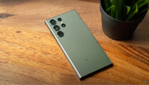 Green smartphone with quad camera array on wooden surface next to potted plant.