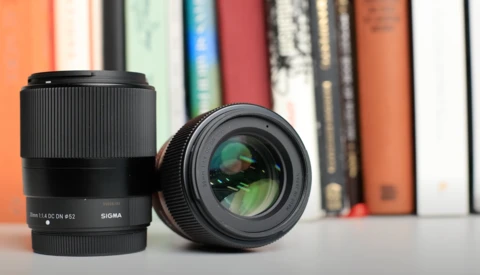 Two Sigma camera lenses displayed on a surface with colorful books in soft focus behind.