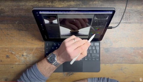Photographer's hand with stylus hovering over tablet displaying image editing software with dual panels.