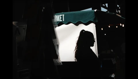 Silhouetted person viewed through a brightly lit storefront window with teal awning at night.