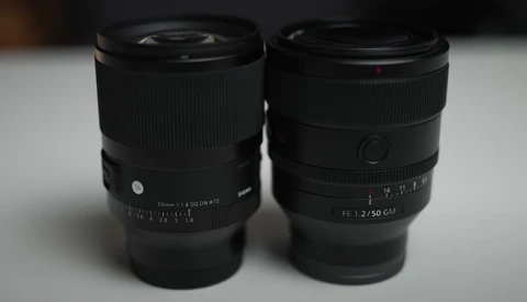 Two black prime lenses side by side on a white surface, displaying focal length markings and aperture rings.