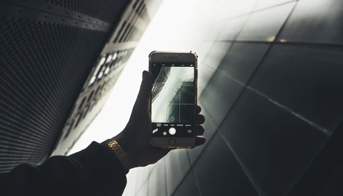 Hand holding smartphone capturing upward view of modern buildings against bright sky.